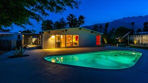 A modern house with a swimming pool, large windows, and a well-lit interior. - Stylish Mid Century Krisel Oasis -New pool deck, Salt Water Pool, Firepit, BBQ (Palm Springs)