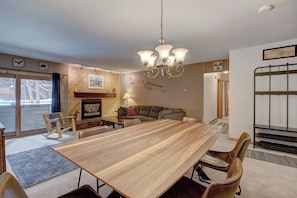 Un salon spacieux avec une table à manger en bois, des fauteuils en cuir, une cheminée et un lustre.