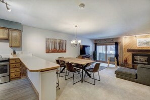 A modern kitchen with a central island, a dining area with a wooden table and chairs, a television, and a fireplace.