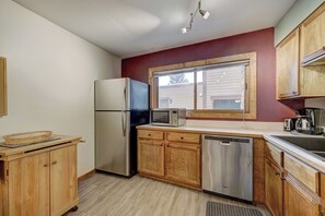 A compact kitchen with wooden cabinets, a stainless steel refrigerator, a microwave, and a dishwasher.