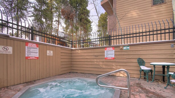 A hot tub area with a wooden fence, caution signs, and a metal railing. - Sundowner II 203 (Breckenridge)