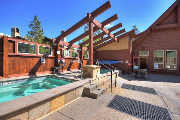 A pool area with a wooden deck, a hot tub, and a covered seating area.