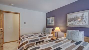 A bedroom with two beds, a wooden dresser, a nightstand with a lamp, and two framed pictures on the wall.