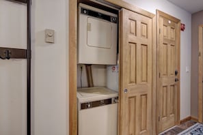 Quarto com máquina de lavar e secar embutidas, portas de madeira e uma tomada elétrica visível.