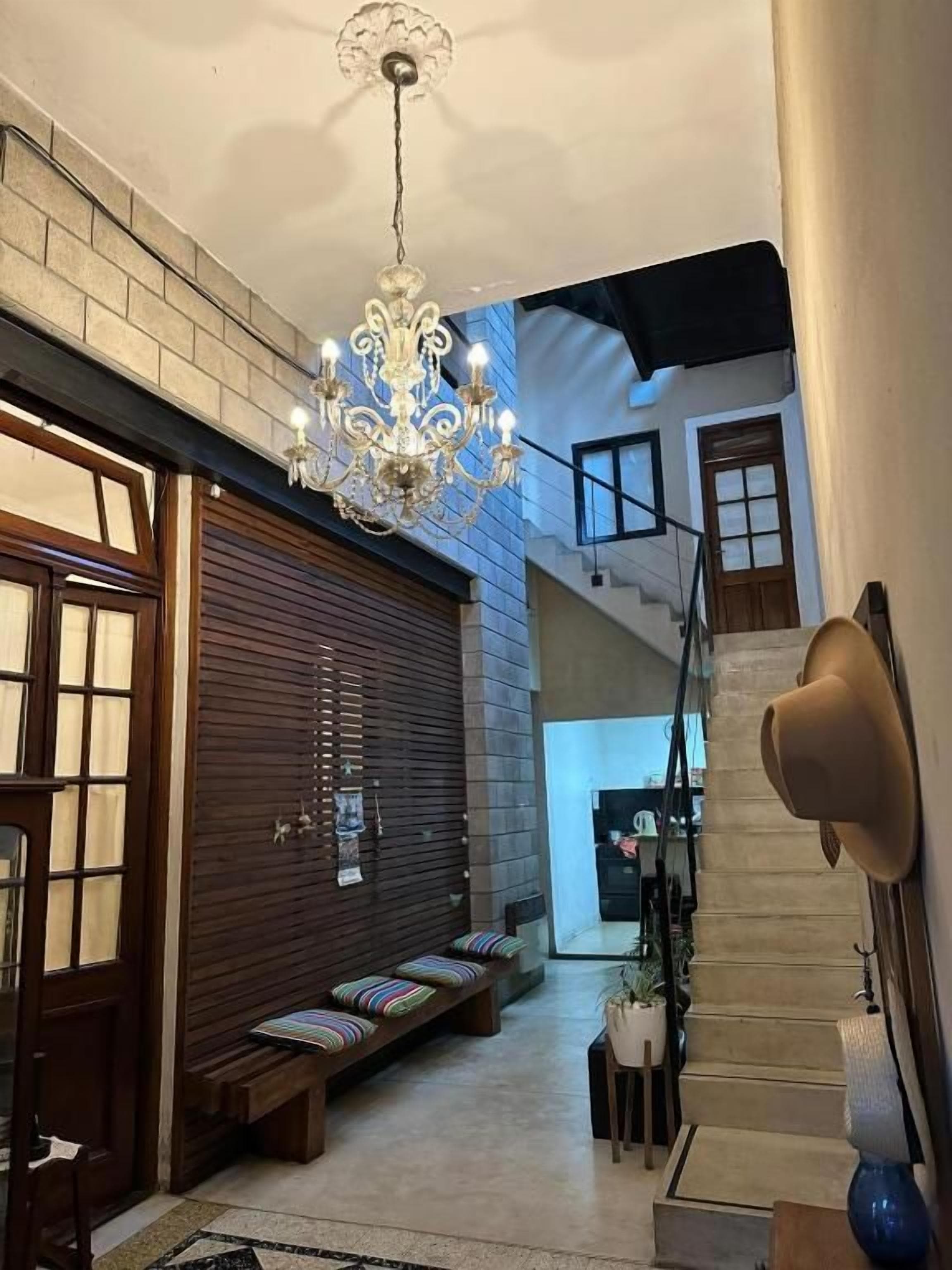 A hallway with a chandelier, wooden benches, a staircase, and a door.