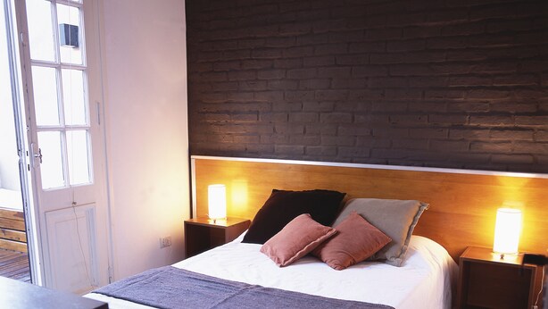 A neatly made bed with a headboard, two bedside lamps, and a window with blinds. - Hostel Carlos Gardel (Buenos Aires)