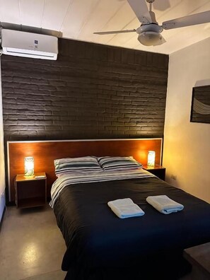 Habitación de hotel con una cama, dos lámparas de noche, un ventilador de techo y un aire acondicionado de pared.