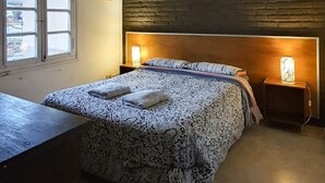 A bedroom with a bed, bedside lamps, a window, and a wall-mounted air conditioner. - Hostel Carlos Gardel (Buenos Aires)