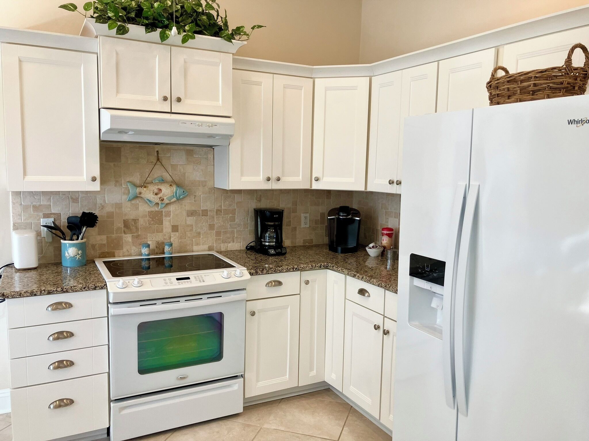 A kitchen with white cabinets, a white refrigerator, a stove, and a coffee maker.