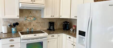 A kitchen with white cabinets, a white refrigerator, a stove, and a coffee maker.