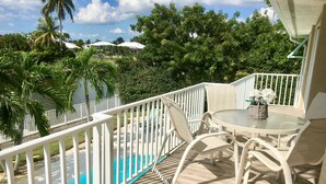 Un espace aménagé au bord de la piscine, avec une clôture blanche, une table ronde entourée de chaises, et une vue sur la piscine et la végétation environnante.