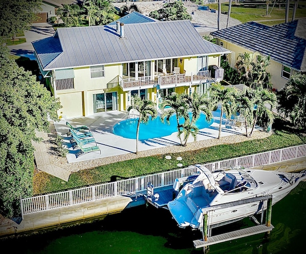 A large house with a swimming pool, a boat dock, and a small bridge.
