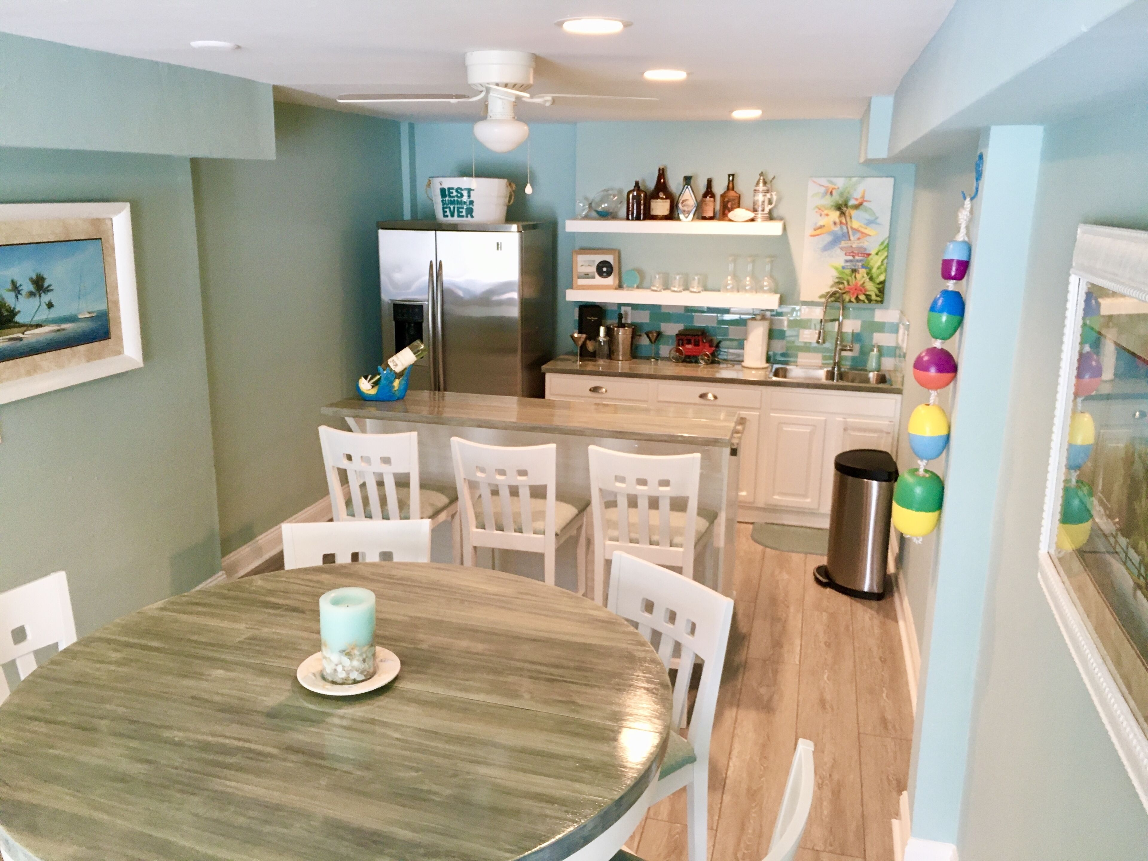 Een kleine keuken met witte kasten, een roestvrijstalen koelkast, en een eethoek met een houten tafel en witte stoelen.