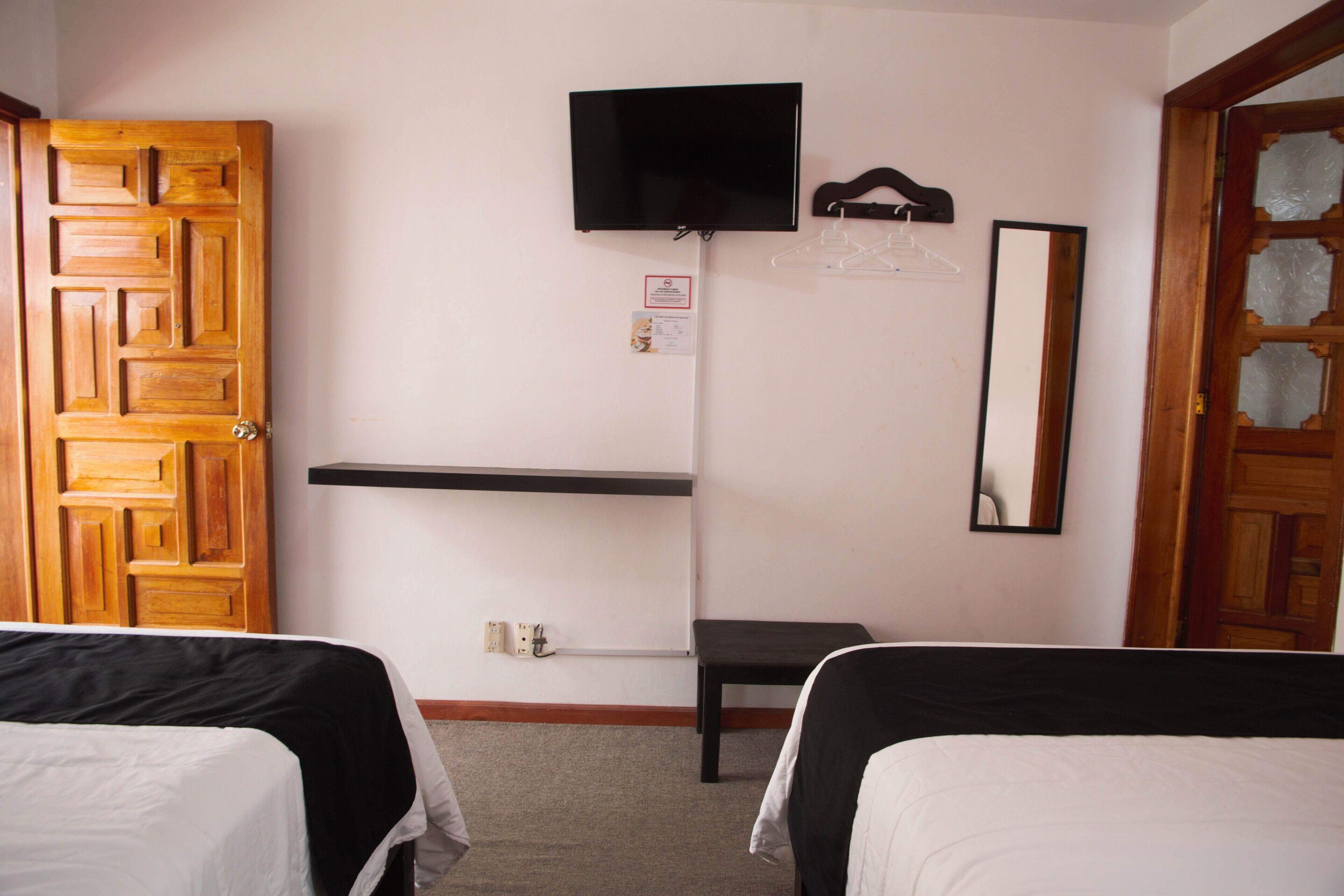Habitación de hotel con dos camas, un televisor montado en la pared, un perchero y un espejo.
