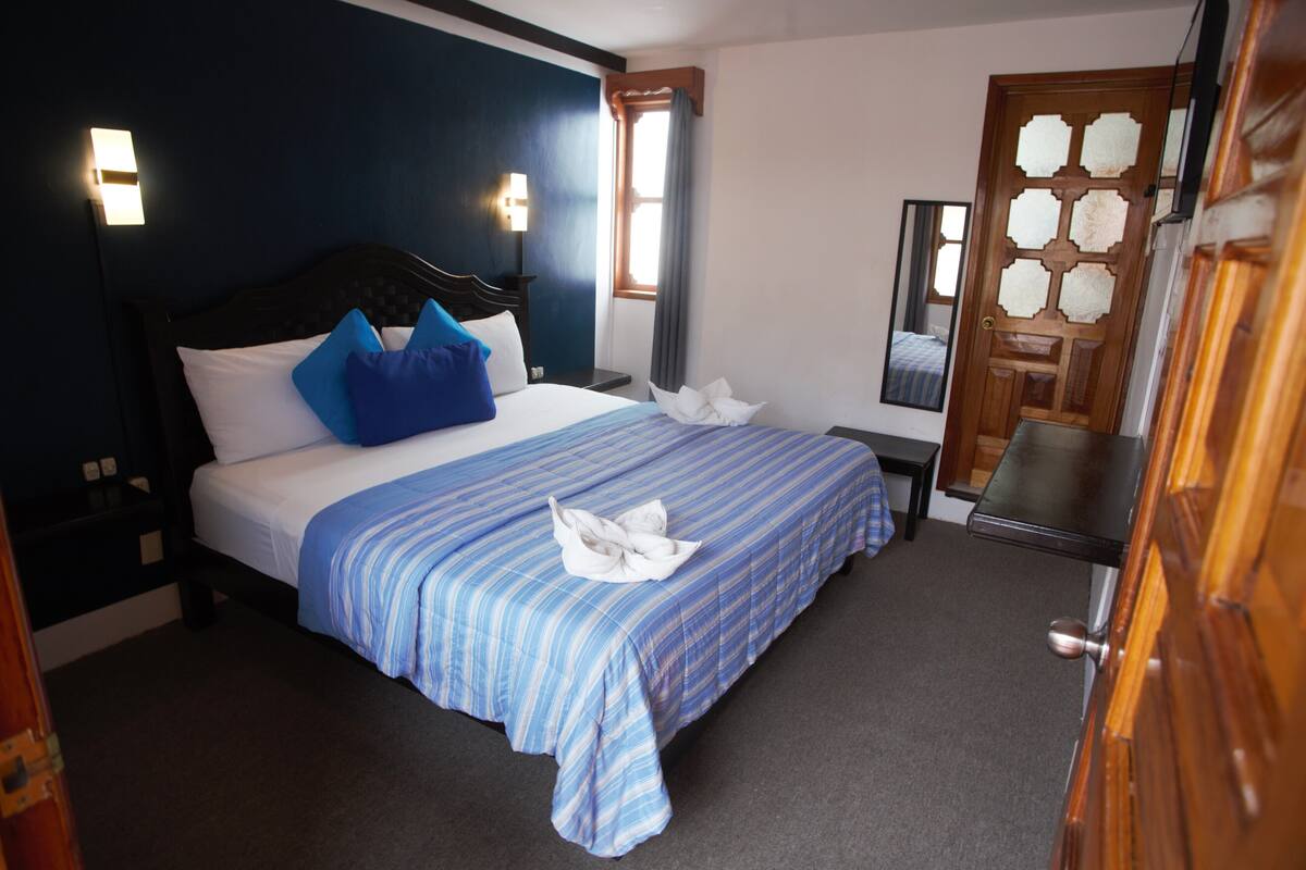 A neatly made bed with blue and white bedding, a wooden headboard, and a bedside table with a lamp.