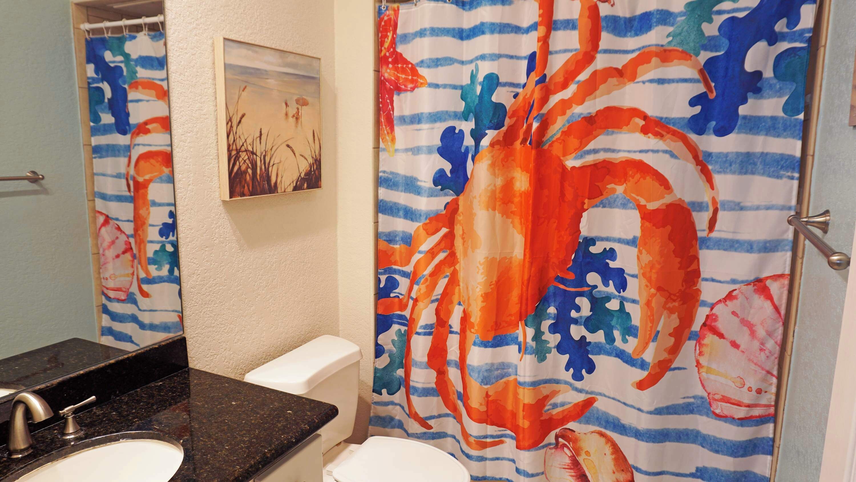 A bathroom with a large mirror, a sink, a toilet, and a shower curtain with a crab design.