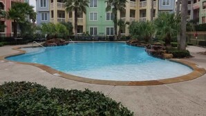 Une piscine entourée d’immeubles à plusieurs étages dotés de balcons, de palmiers et d’un espace paysager.