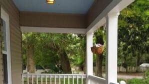 A covered porch with a white railing, a hanging planter, and a light fixture.
