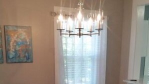 A dining area with a round table, six chairs, a chandelier, and a bench.