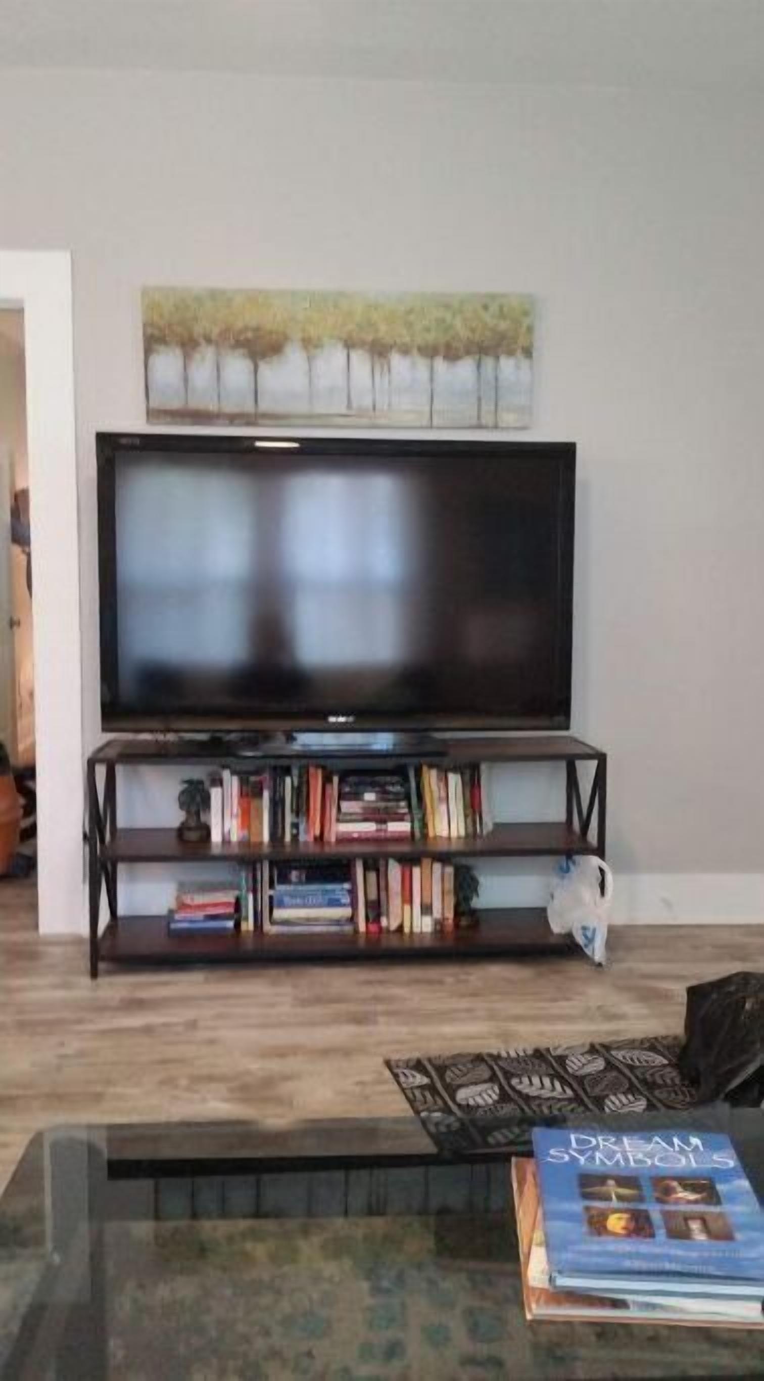 A living room with a flat-screen TV on a stand, a bookshelf with various books, and a coffee table with a magazine.