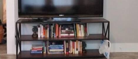 A living room with a flat-screen TV on a stand, a bookshelf with various books, and a coffee table with a magazine.