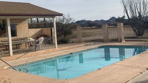 Une piscine avec un patio couvert, une cour clôturée et un paysage montagneux en arrière-plan.