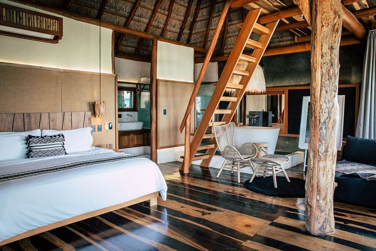A spacious bedroom with a large bed, a wooden staircase, and a seating area with wicker chairs.