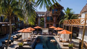 A pool area with lounge chairs, umbrellas, and a thatched-roof building. - Aldea Kuká, Luxury Eco Boutique Hotel  (Isla Holbox)