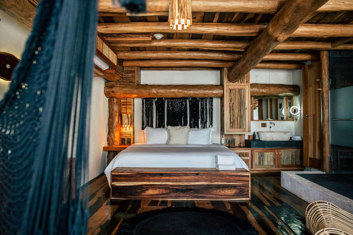 A rustic wooden bedroom with a large bed, a wooden headboard, a bedside table with a lamp, and a built-in bench.