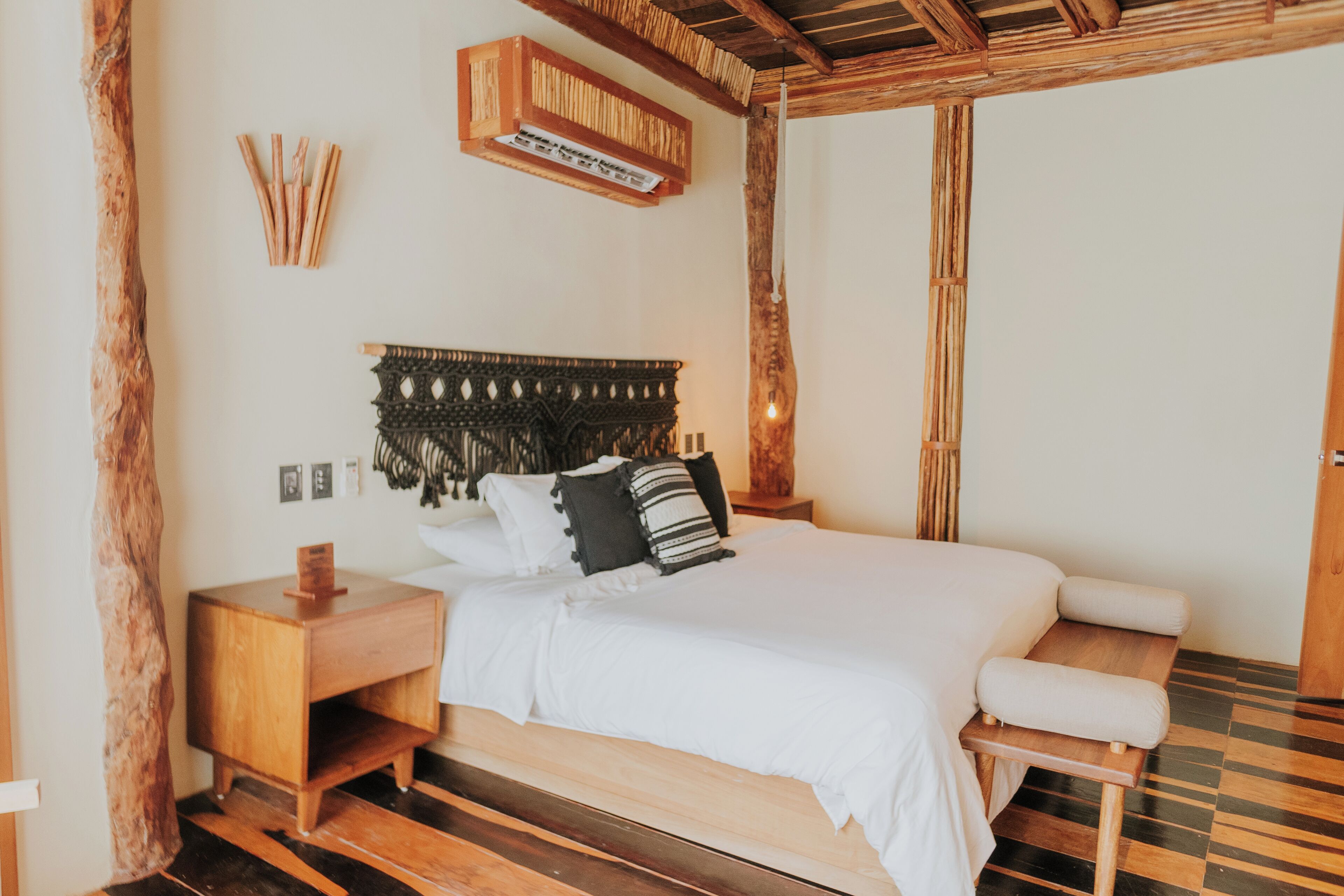 Une chambre avec un lit en bois, une table de chevet, un banc et une étagère fixée au mur.