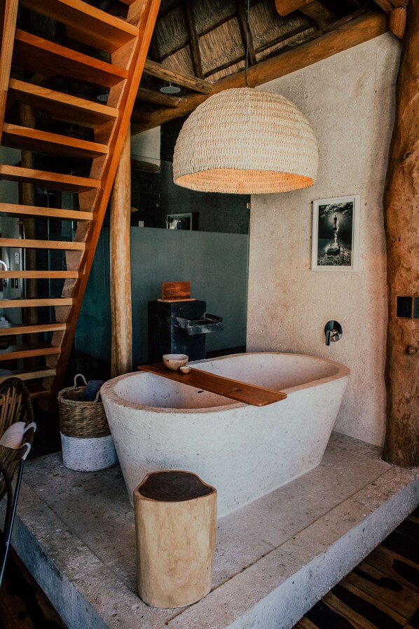 A rustic bathroom with a large bathtub, wooden ladder, and a woven light fixture.
