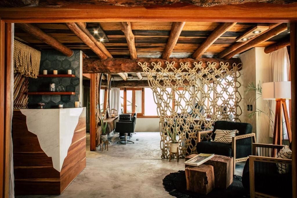 Um interior rústico com vigas de madeira aparentes, parede de pedra, divisória de tecido e um espaço de estar aconchegante com sofá e poltronas.
