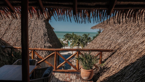 A wooden deck with a thatched roof, overlooking a beach and palm trees. - Aldea Kuká, Luxury Eco Boutique Hotel  (Isla Holbox)