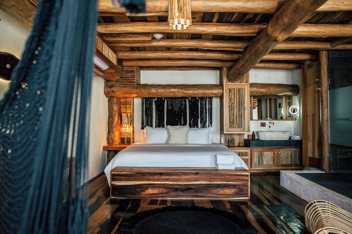 A rustic bedroom with a wooden bed, a small vanity, and a large window.