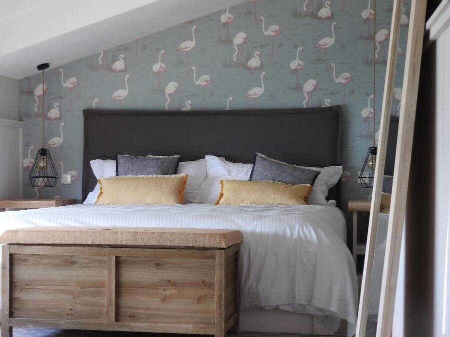 Un dormitorio con una cama grande, cabecera de madera y un papel tapiz con estampado de flamencos.