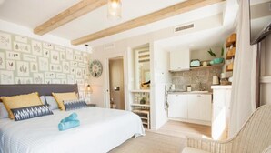 A bedroom with a bed, a chair, a kitchen area, and a dining table. - The Beach House - Studios & Suites (Javea)