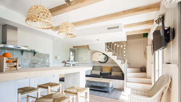 A modern kitchen with a bar area, wicker chairs, and a staircase leading to another level. - The Beach House - Studios & Suites (Javea)