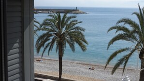 A beach view with palm trees and a pier in the distance. - The Beach House - Studios & Suites (Javea)