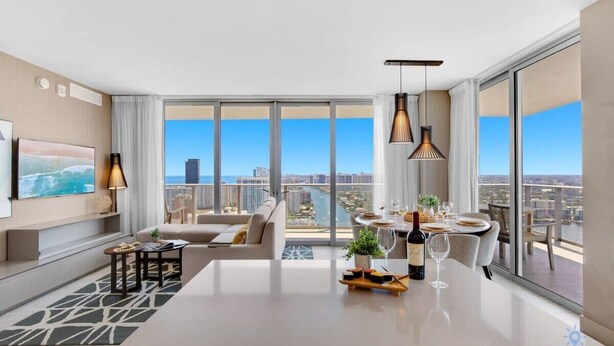 A modern living room with a large window, a dining area, and a sofa. - Luxury w/ stunning view |Balcony |Amazing Pools (Hollywood)