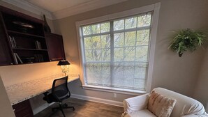 Ein Homeoffice mit Schreibtisch, Stuhl und einem großen Fenster mit Jalousien.