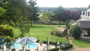 A pool area with lounge chairs and umbrellas, surrounded by a well-maintained lawn and a stone wall. - Luxury gites & B&B, near Saumur, in 18thC former wine estate, heated pool  (Les Bois D'anjou, Pays De La Loire)