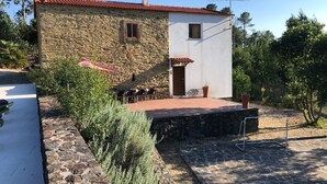 Une maison en pierre avec un toit recouvert de tuiles rouges, un petit porche avec des chaises et un jardin.