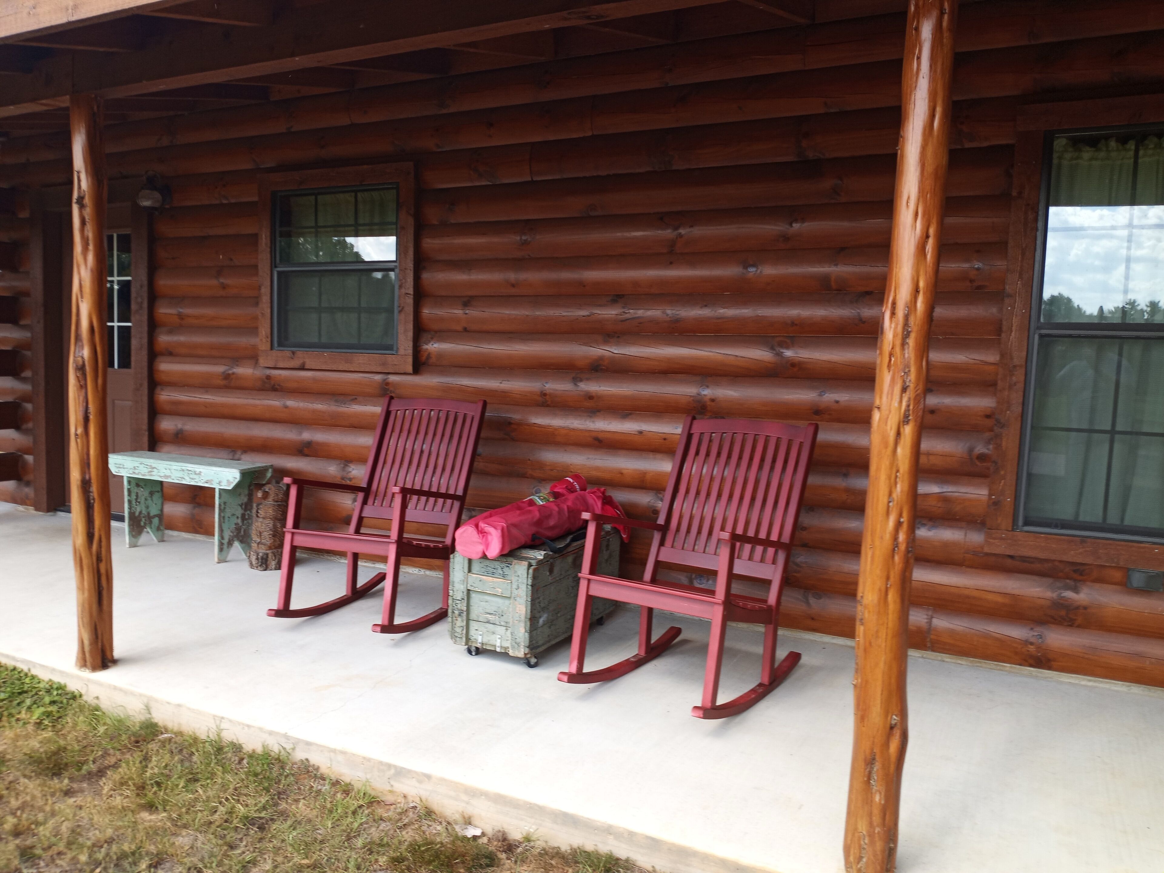 Une cabane en rondins avec deux fauteuils à bascule et une petite table à l’extérieur.