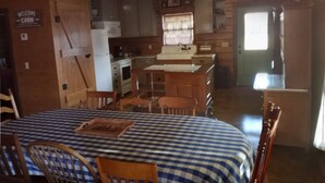 L’intérieur d’une cabane est aménagé avec une table à carreaux, des chaises en bois, un coin cuisine comprenant un réfrigérateur, une cuisinière et un évier, ainsi qu’une pancarte indiquant « Bienvenue à la cabane ».