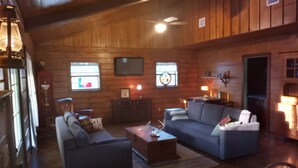 Un salon chaleureux avec des murs en bois, un ventilateur de plafond, une cheminée et un téléviseur fixé au mur.