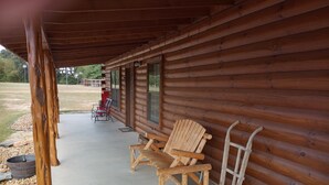 Une cabane en bois avec une véranda, deux fauteuils Adirondack et une brouette.