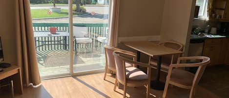A room with a sliding glass door leading to an outdoor patio area. Inside, there is a wooden table with two chairs and a small wooden desk with a chair.
