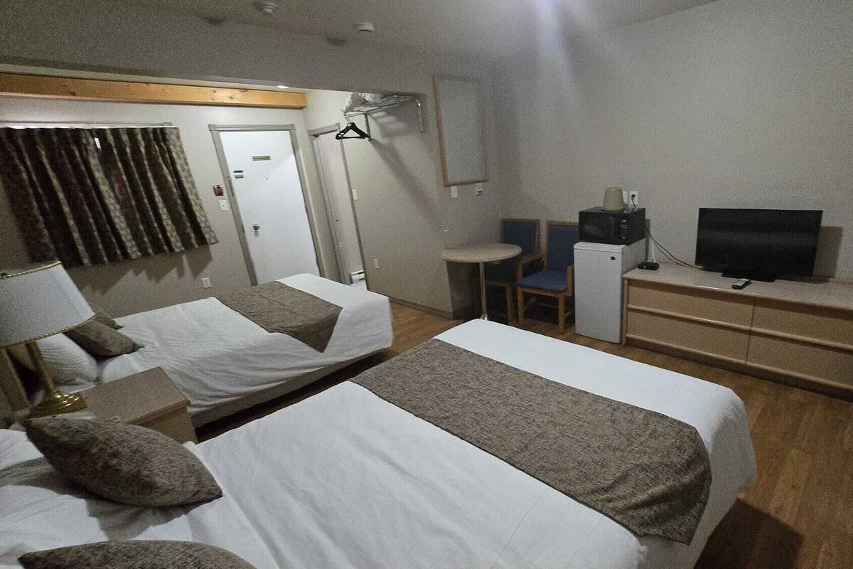 A hotel room with two beds, a television, a small table, and a cabinet.