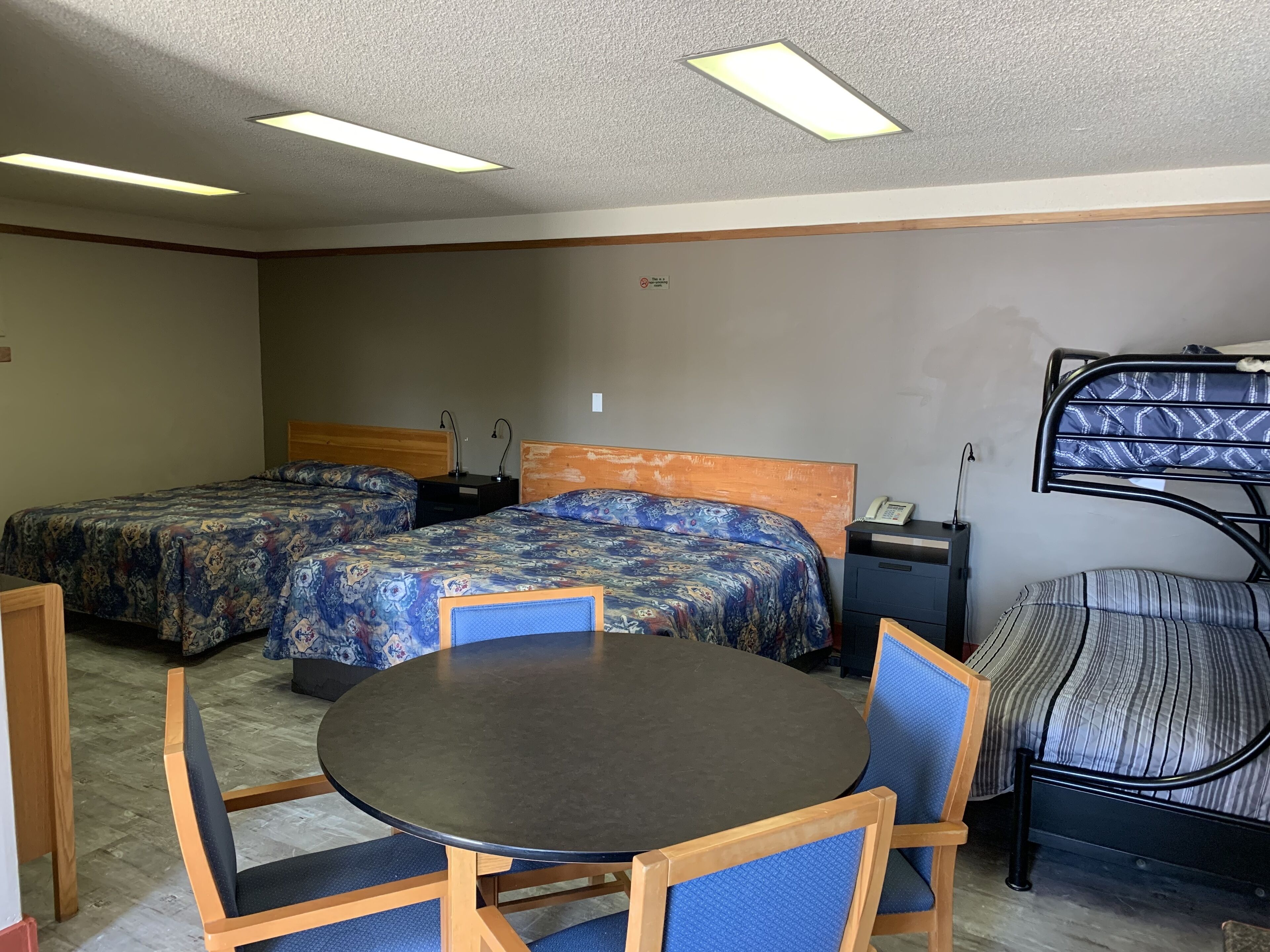 A hotel room with two beds, a round table, and a bunk bed.