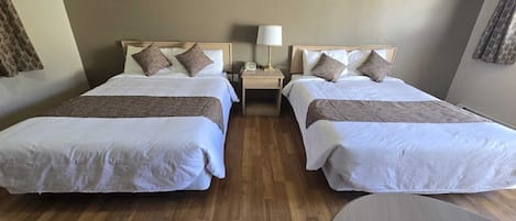 Een hotelkamer met twee bedden, een nachtkastje met een lamp en een ronde tafel.